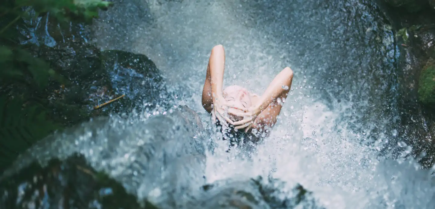 Woman under a waterfall feeling pain-free.